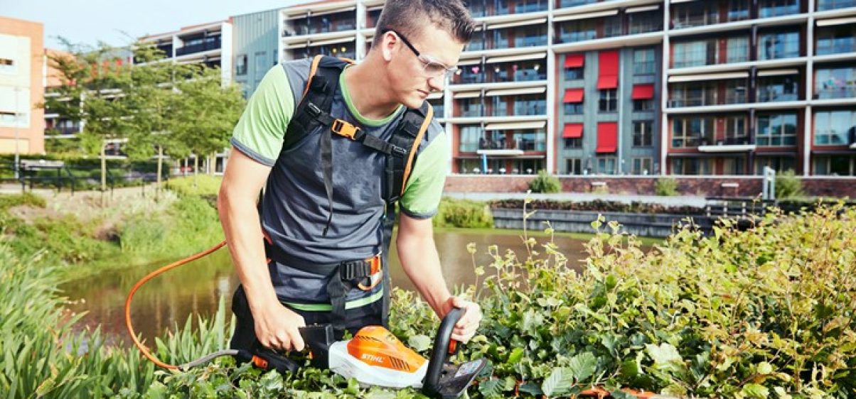 Een medewerker van Donker Groen verzorgt het groen in Delfshaven met elektrisch gereedschap.